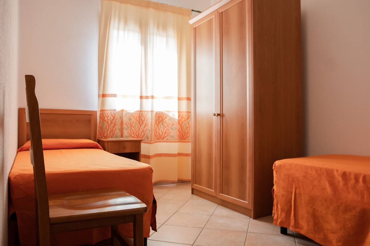 Una camera da letto con due letti, un armadio in legno, un comodino e una sedia.
