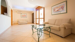 A spacious living room with a glass coffee table, a beige sofa, and a framed painting on the wall. - Violet Residence In Orosei (Orosei)