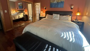 Een slaapkamer met een groot bed, een plafondventilator, een schilderij aan de muur en een spiegel die de kamer weerkaatst.