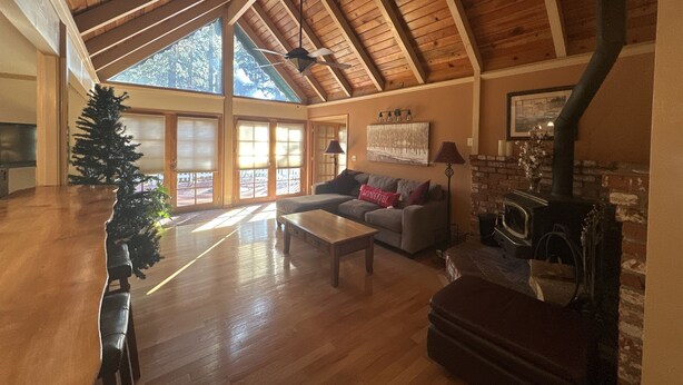 Een ruime woonkamer met een hoge plafond, houten balken, een open haard en een groot raam.
