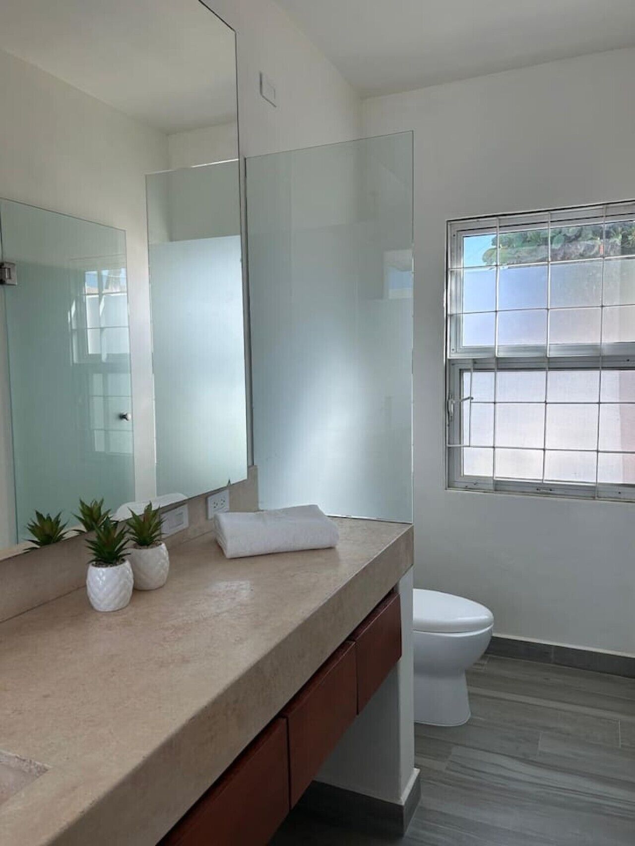 A modern bathroom with a large mirror, a toilet, and a window.