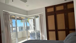 Ein Schlafzimmer mit einem Bett, einer Glasschiebetür, die auf einen Balkon führt, und einem Holzschrank.