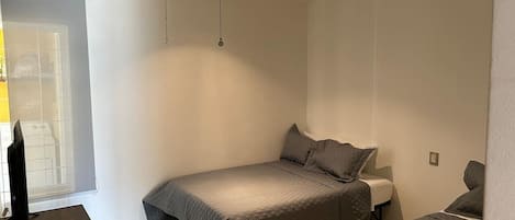 Un dormitorio con cama, escritorio, silla, ventilador de techo y ventana.