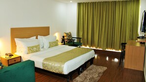 A hotel room with a bed, bedside table, lamp, green chair, desk, and a ceiling fan. - HOTEL THE GOLDEN SANDS (Calangute)