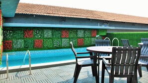 A poolside area with a tiled roof, a pool, and a seating arrangement with chairs and a table. - HOTEL THE GOLDEN SANDS (Calangute)