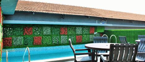 A poolside area with a tiled roof, a pool, and a seating arrangement with chairs and a table.