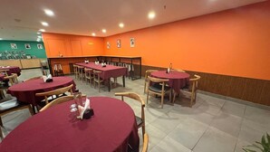 A restaurant with round tables covered in red tablecloths, wooden chairs, and orange walls. - HOTEL THE GOLDEN SANDS (Calangute)