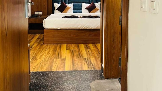 A bedroom with a bed, wooden flooring, a ceiling fan, and a nightstand. - Hotel Swarn Bhoomi (Kanpur)
