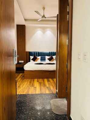 A bedroom with a bed, wooden flooring, a ceiling fan, and a nightstand. - Hotel Swarn Bhoomi (Kanpur)