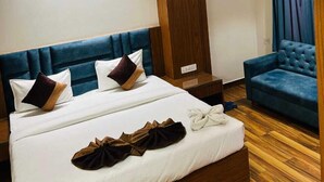 A hotel room with a large bed, a blue upholstered sofa, a wooden floor, and a ceiling fan. - Hotel Swarn Bhoomi (Kanpur)