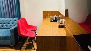 A compact room with a wooden dining table, two red chairs, a blue sofa, and a large mirror on the wall. - Hotel Swarn Bhoomi (Kanpur)