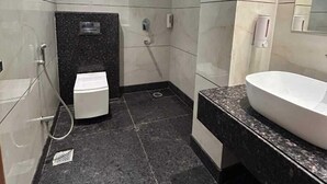 A bathroom with a black marble floor, a white sink, and a shower. - Hotel Swarn Bhoomi (Kanpur)