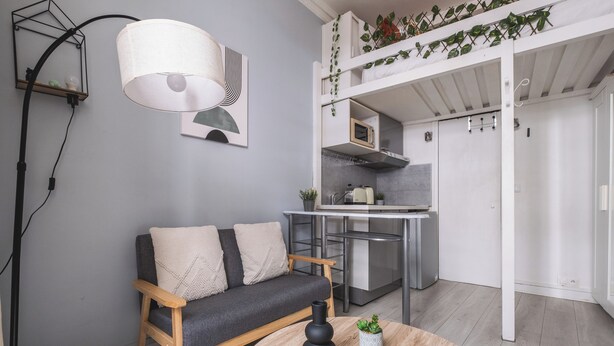 A modern living space with a sofa, coffee table, and kitchen area. - Charmant studio au cœur du 16 (Paris)