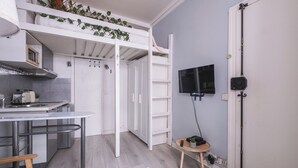 A compact kitchen with a built-in stove, a small dining table, and a TV mounted on the wall. - Charmant studio au cœur du 16 (Paris)