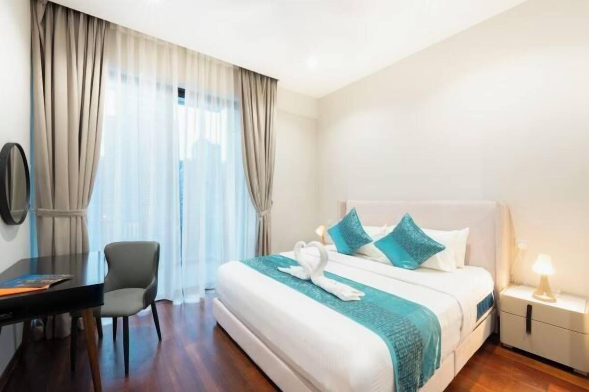 Quarto de hotel com cama, escrivaninha, cadeira e mesa de cabeceira.