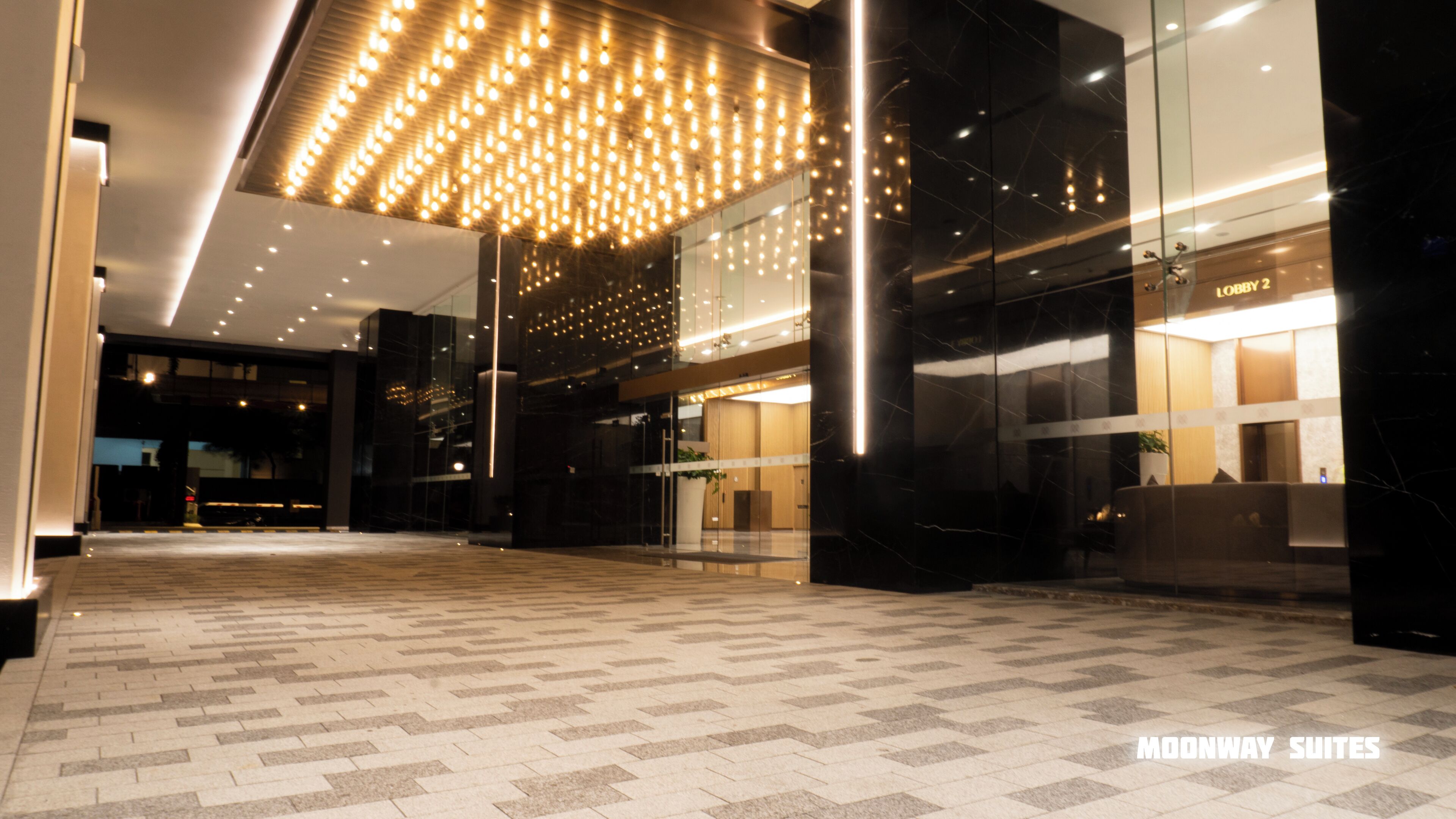 A modern lobby with a patterned floor, a glass entrance, and a ceiling with hanging lights.