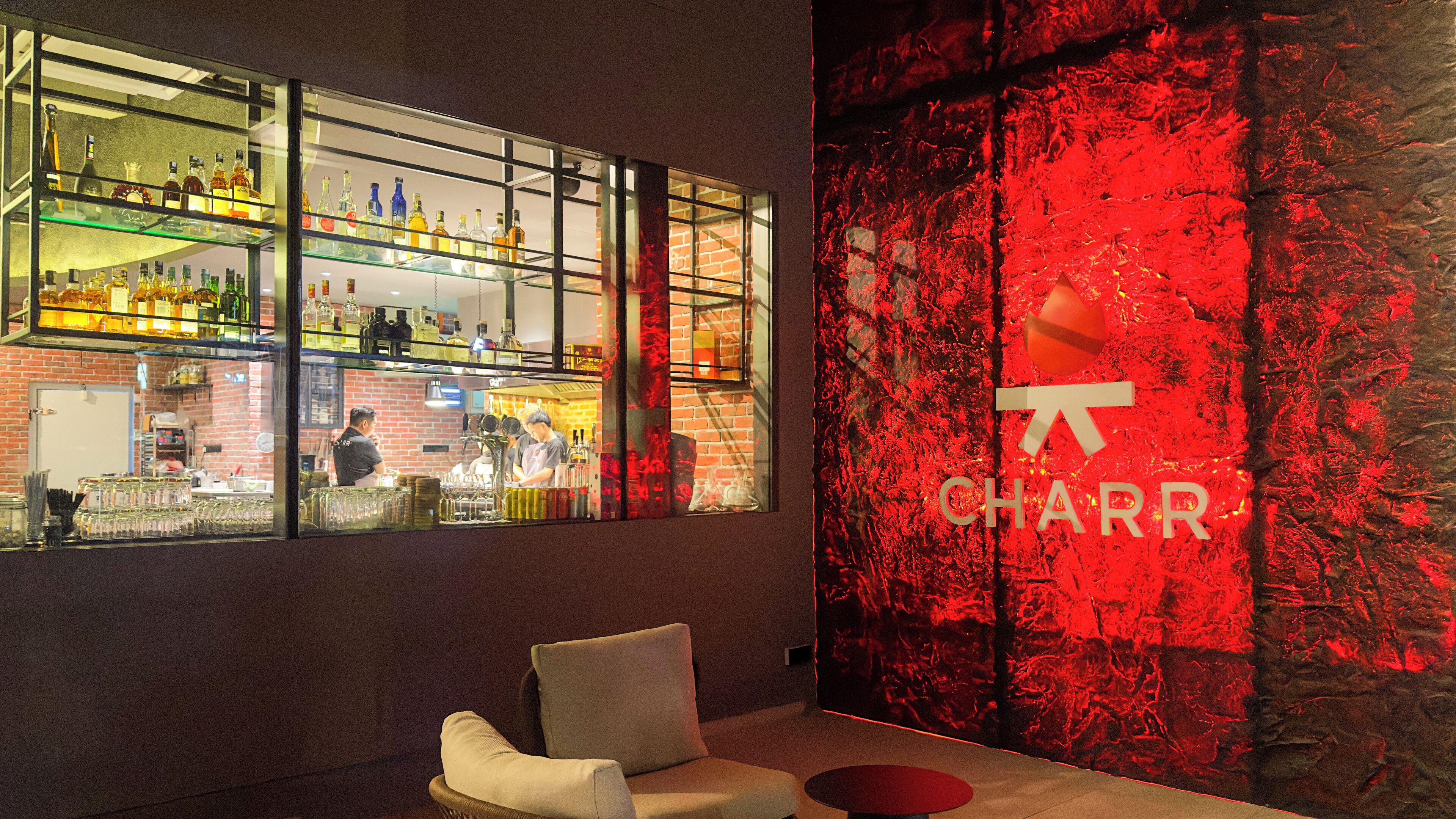 A bar area with shelves of bottles, a seating area with a chair, and a red textured wall with the word "CHARR" visible.