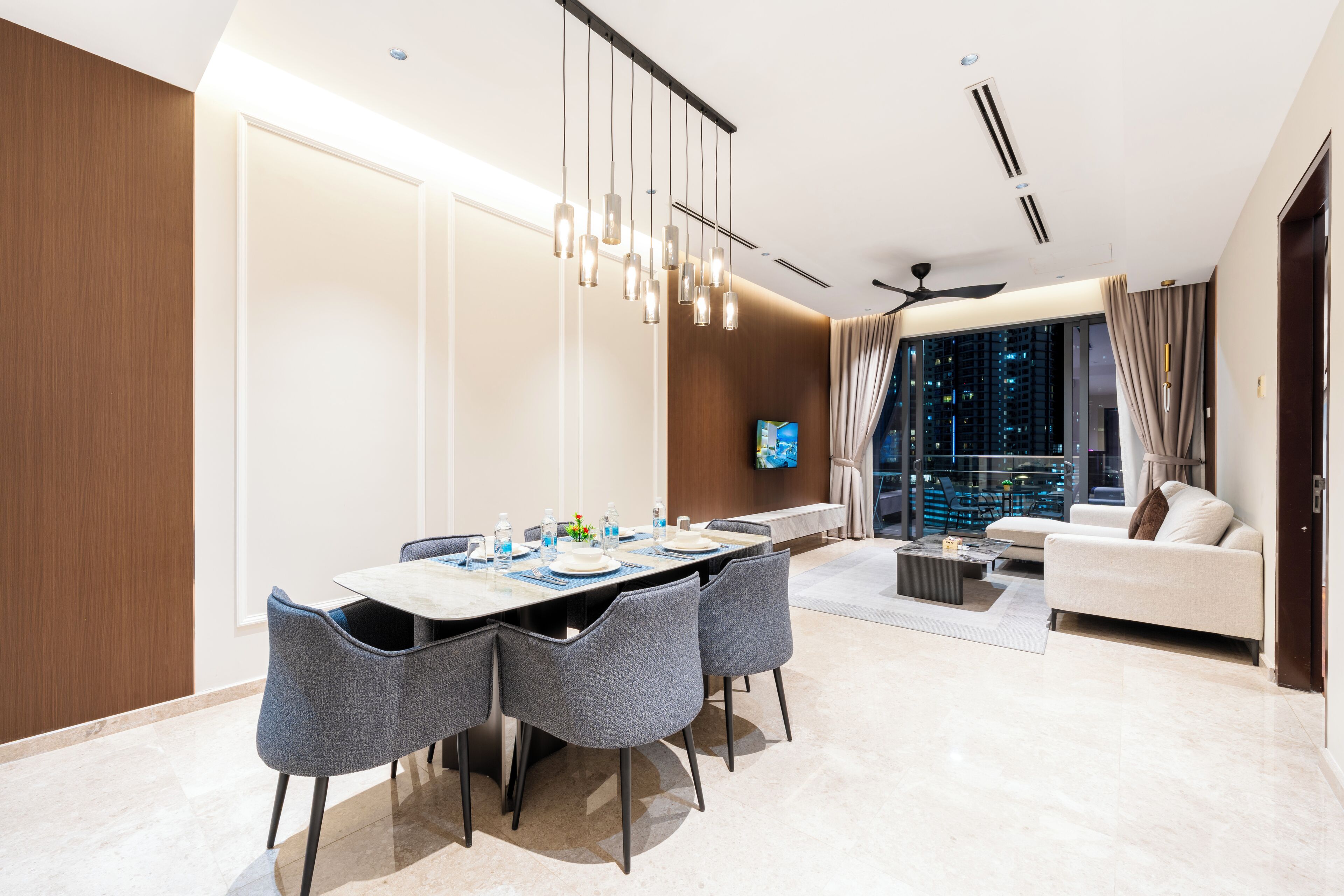 A modern hotel room with a dining area, a sofa, and a view of the city at night.
