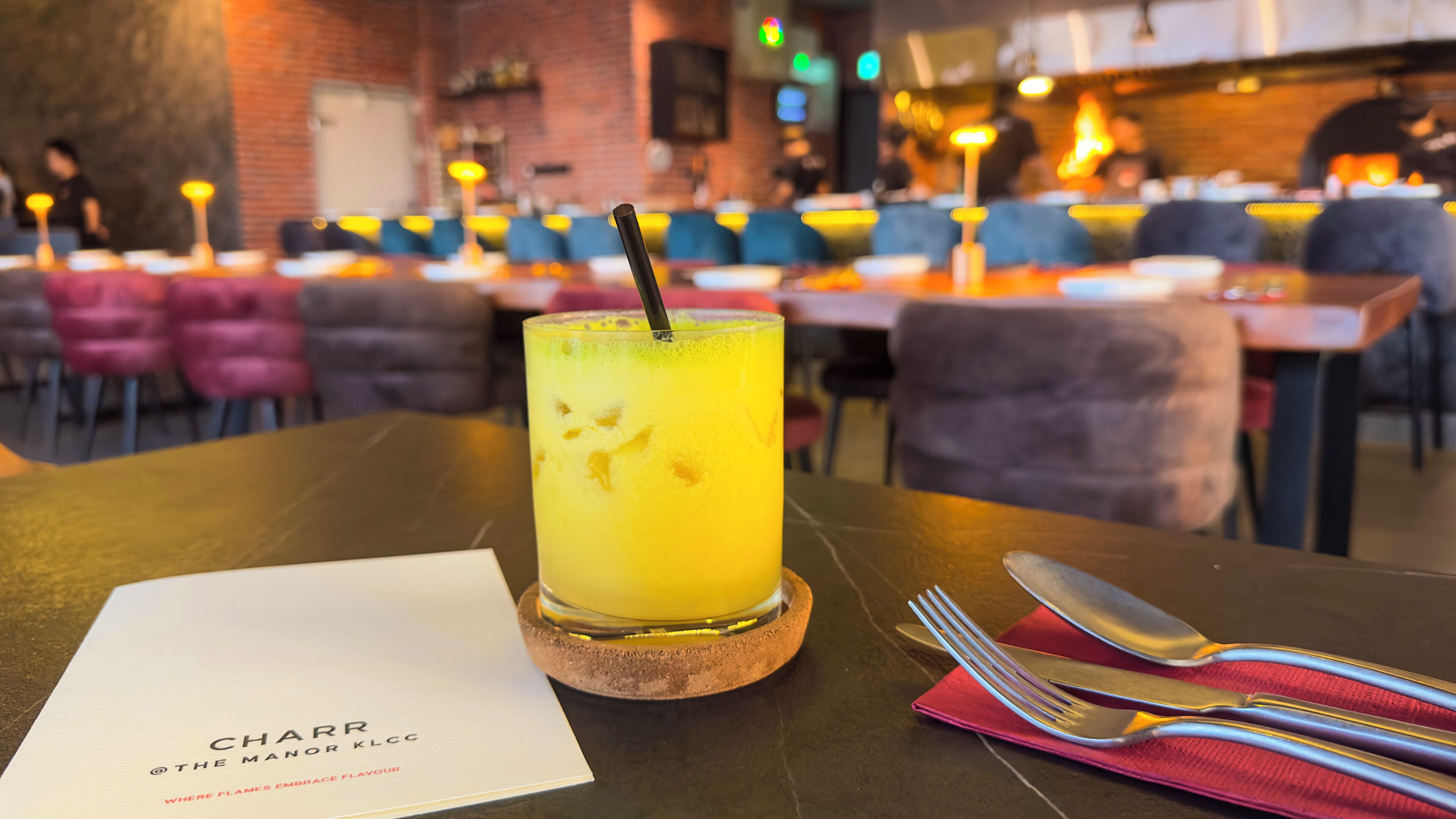 Un restaurante con una mesa dispuesta para comer, mostrando un menú y un vaso de una bebida amarilla.