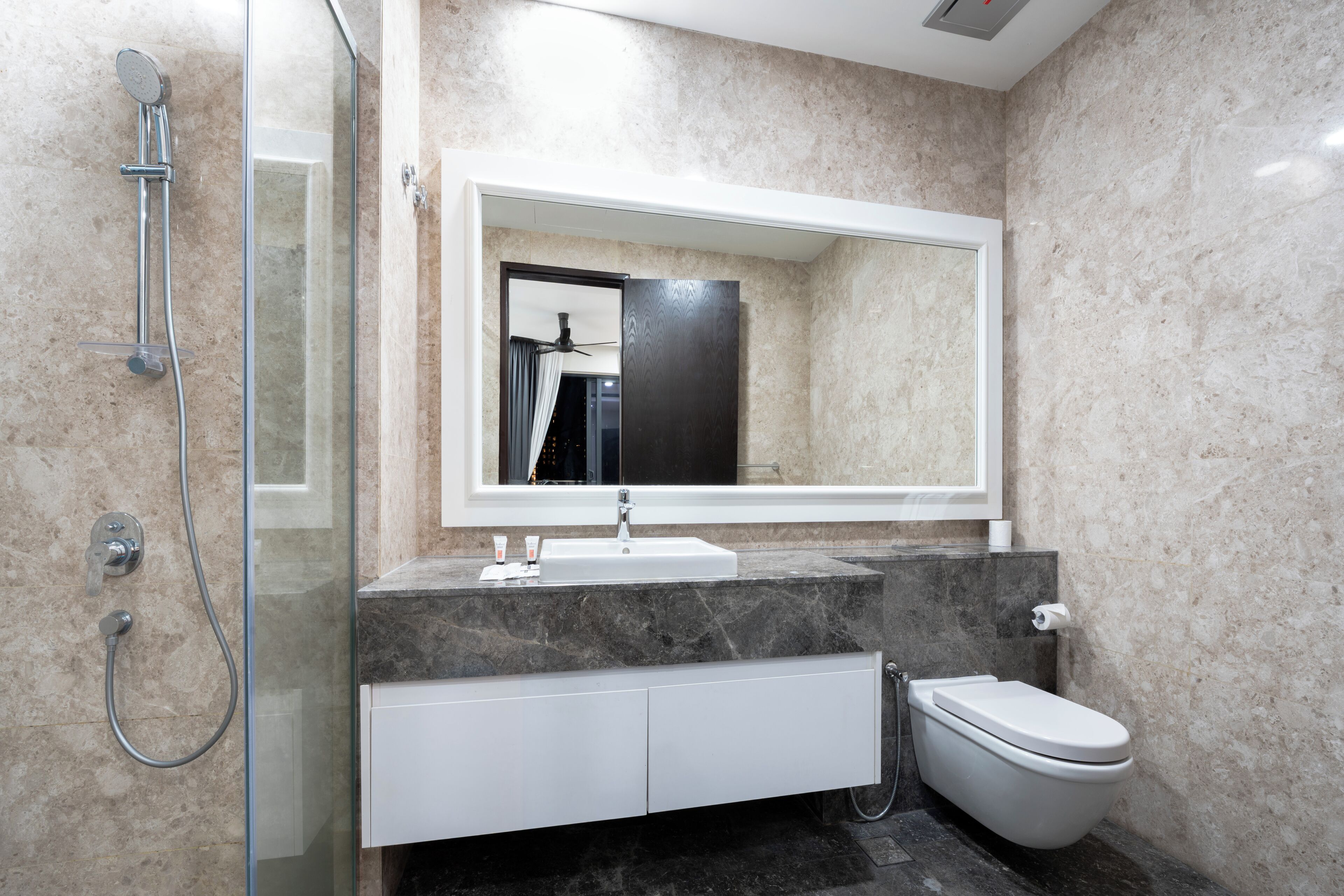 A modern bathroom with a glass-enclosed shower, a white sink, a large mirror, and a toilet.