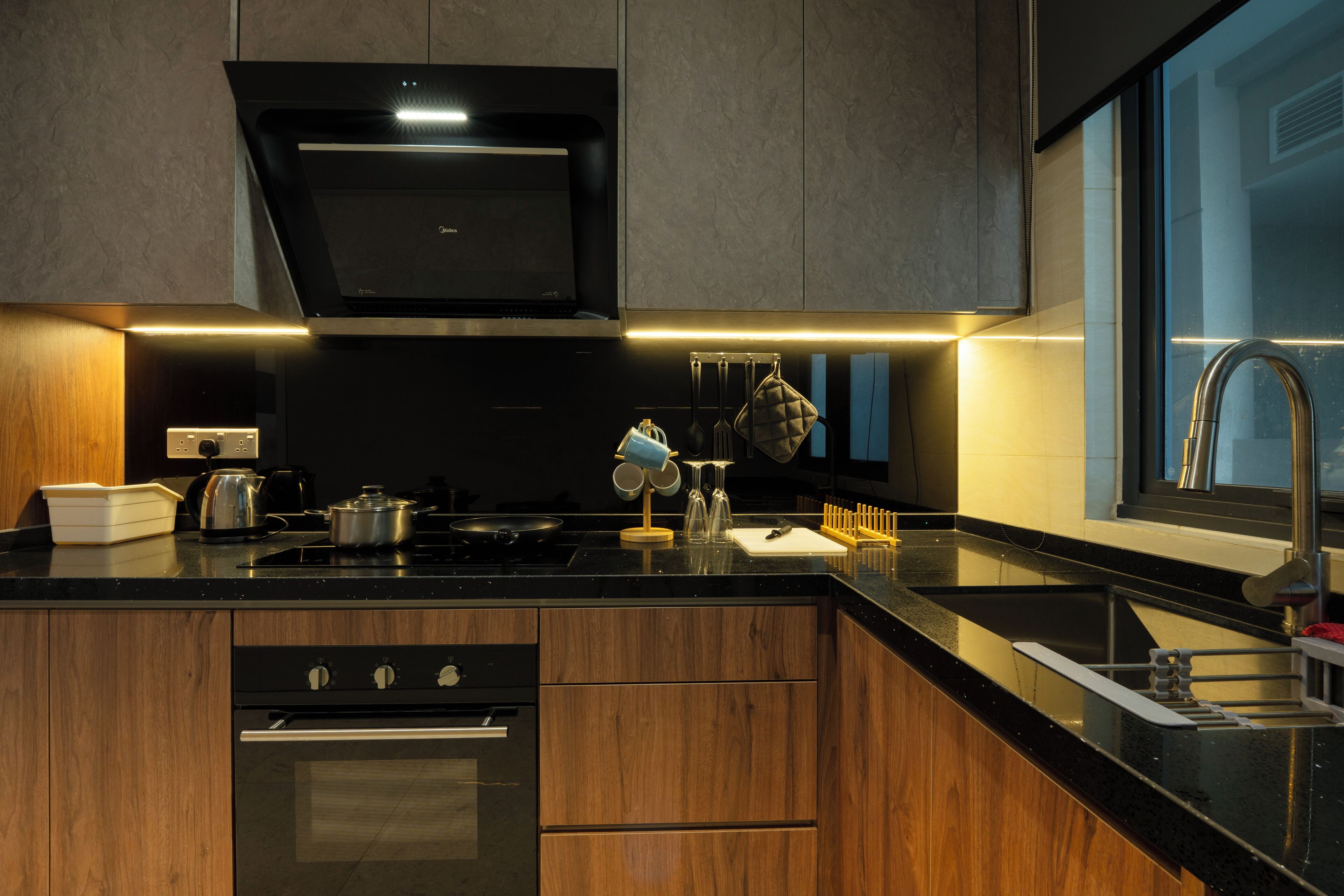 Une cuisine moderne avec des meubles en bois, une cuisinière en acier inoxydable et un plan de travail noir.