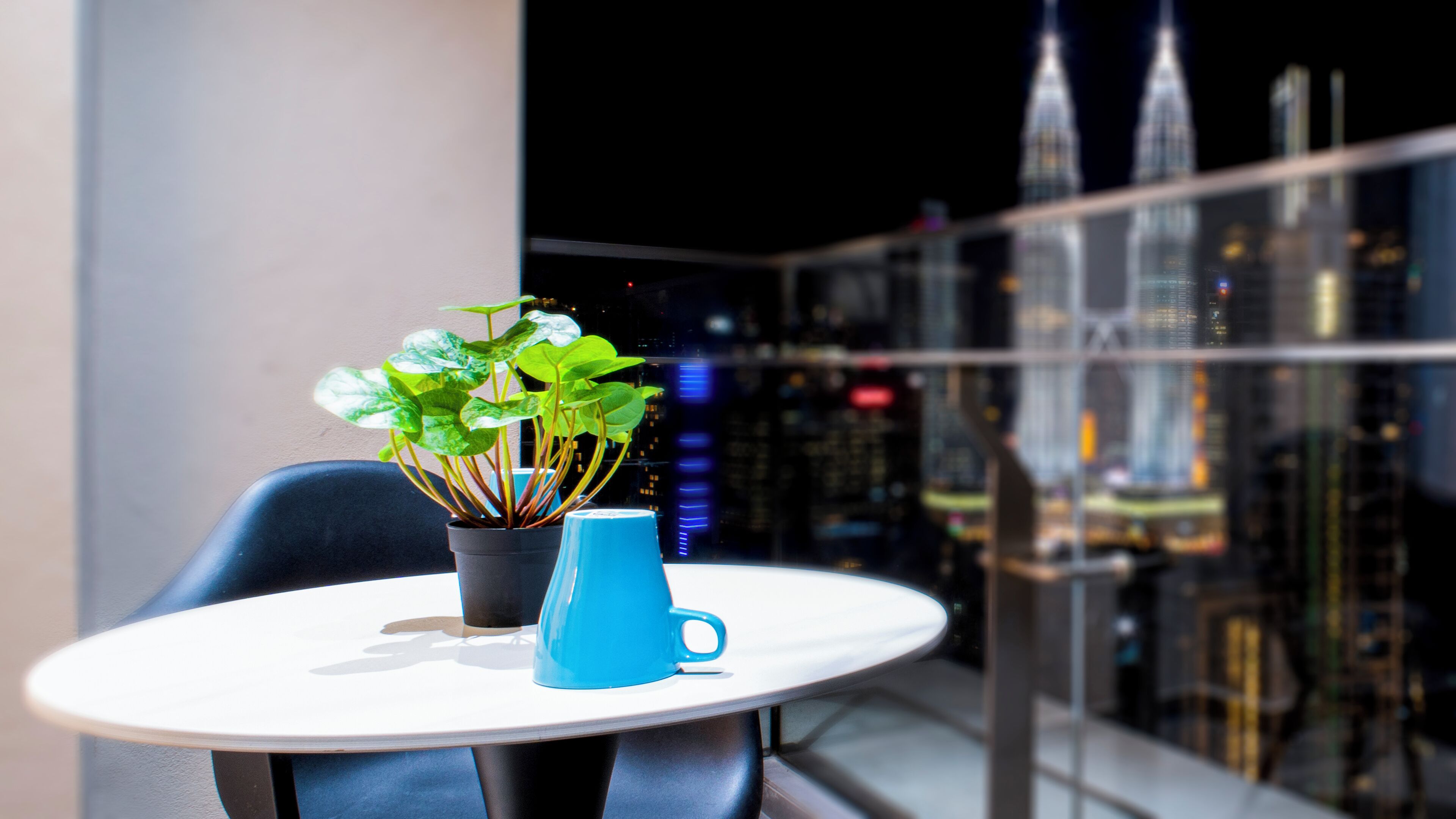 A balcony with a table, a potted plant, and a blue mug.
