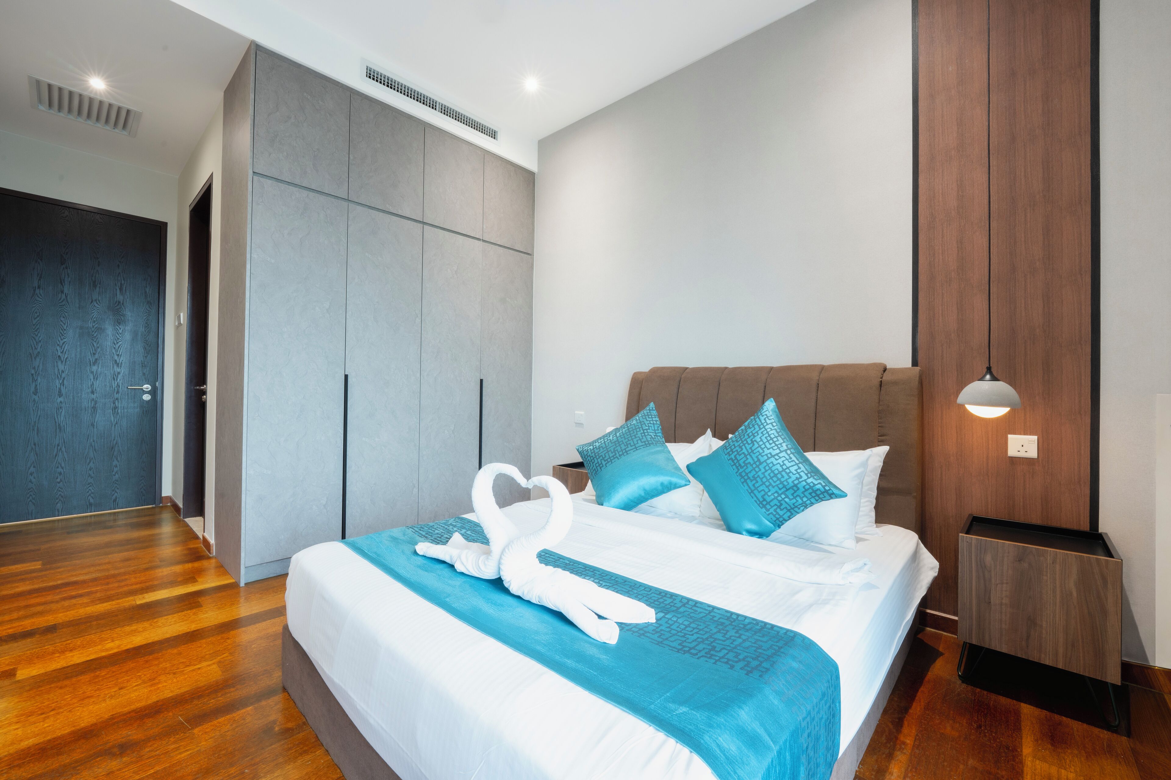 A modern hotel room with a large bed, a wardrobe, a nightstand, and a wall-mounted lamp.