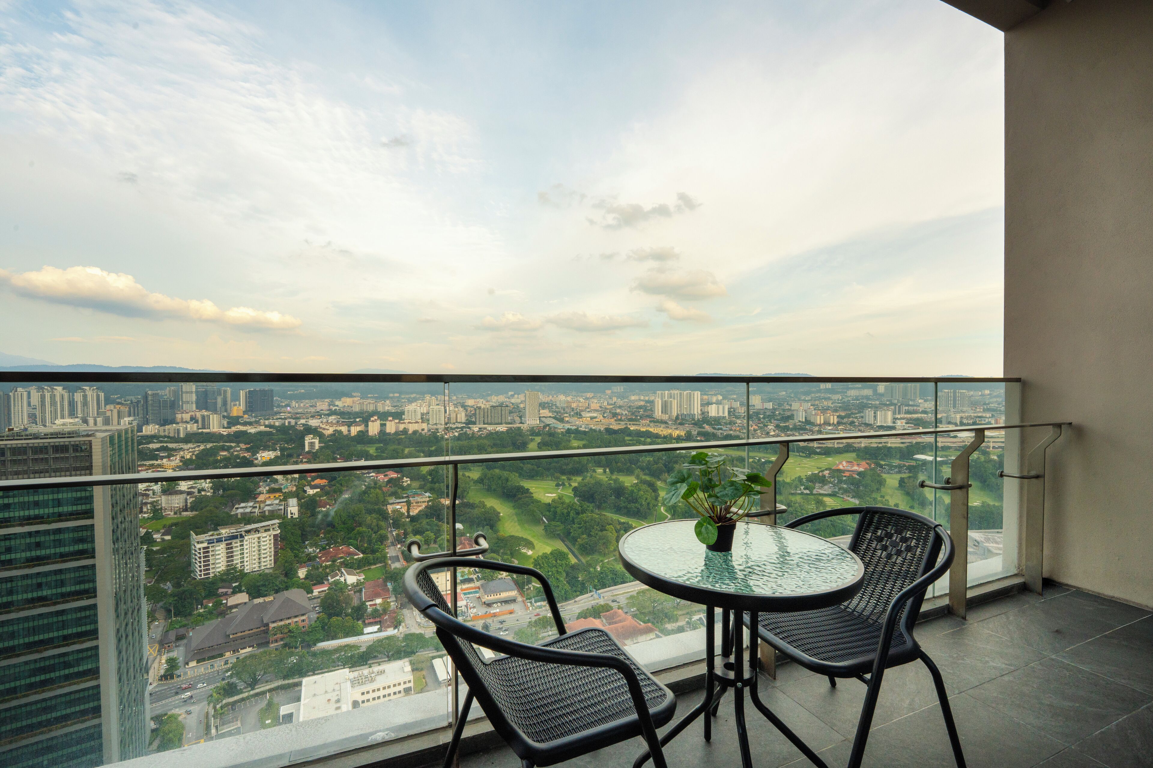 A balcony with a glass railing, two chairs, a small table, and a potted plant.