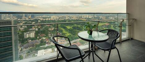 A balcony with a glass railing, two chairs, a small table, and a potted plant.