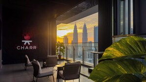 Un salon moderne offrant une vue sur les tours Petronas au coucher du soleil, avec des sièges confortables et une grande fenêtre.