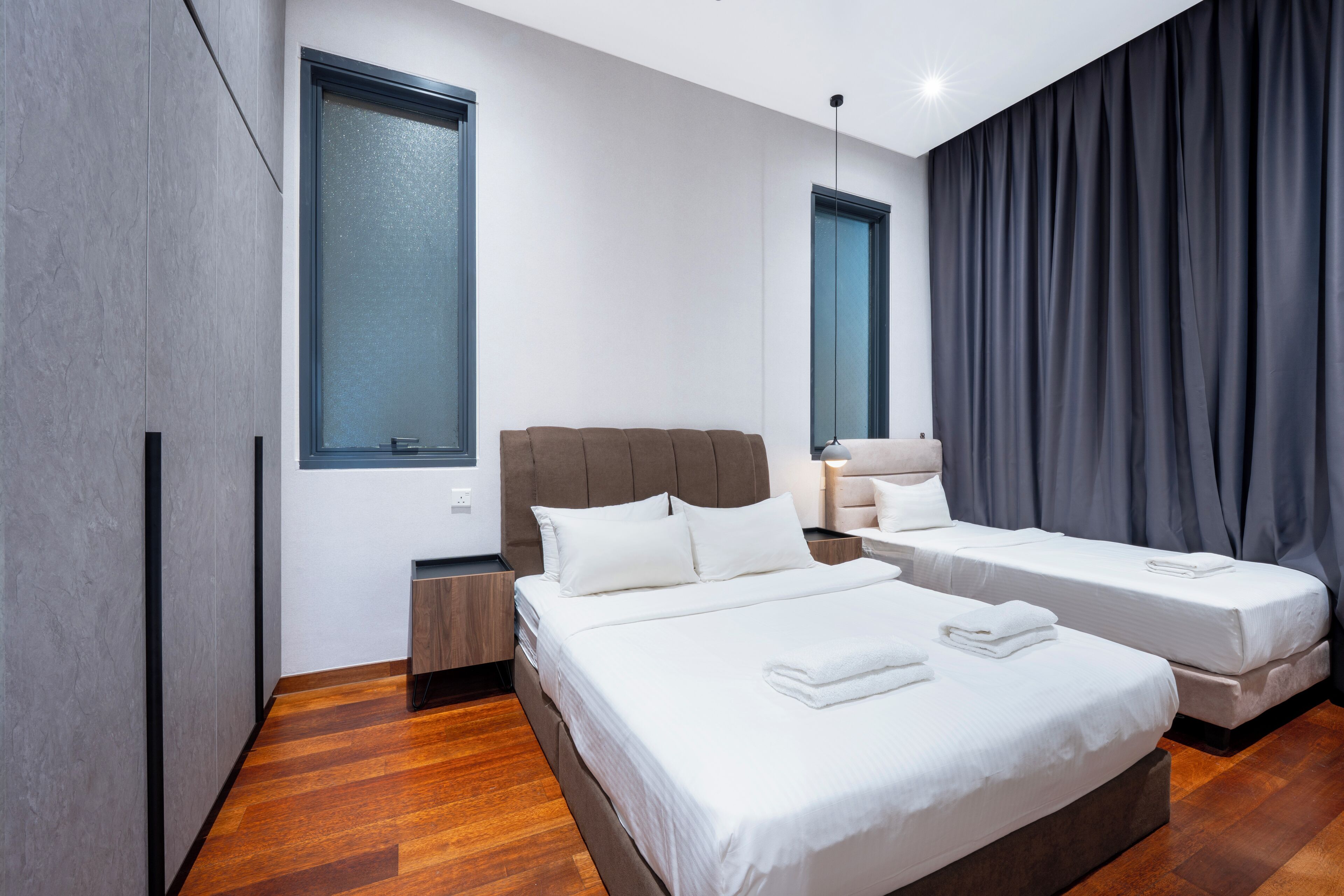 Habitación de hotel moderna con dos camas, un ventanal grande y una cortina oscura.