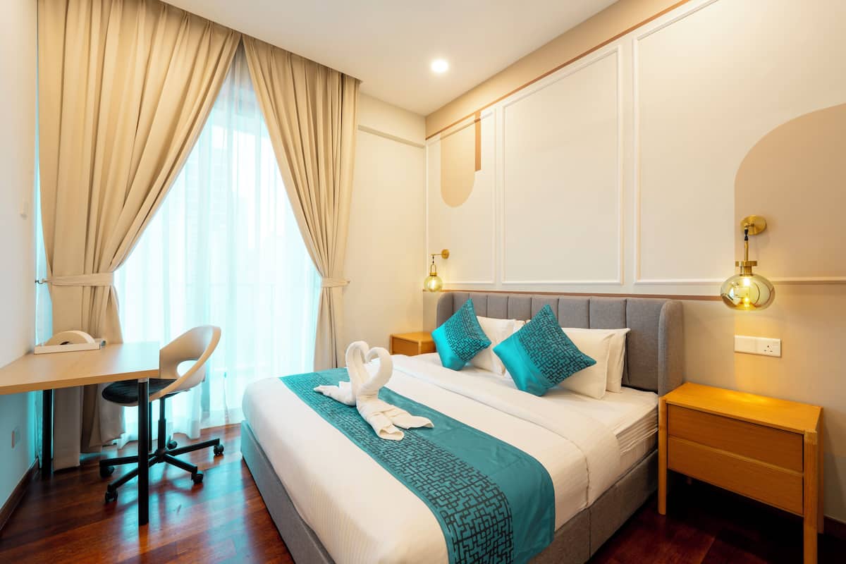 Quarto de hotel com cama, escrivaninha, cadeira e mesa de cabeceira.