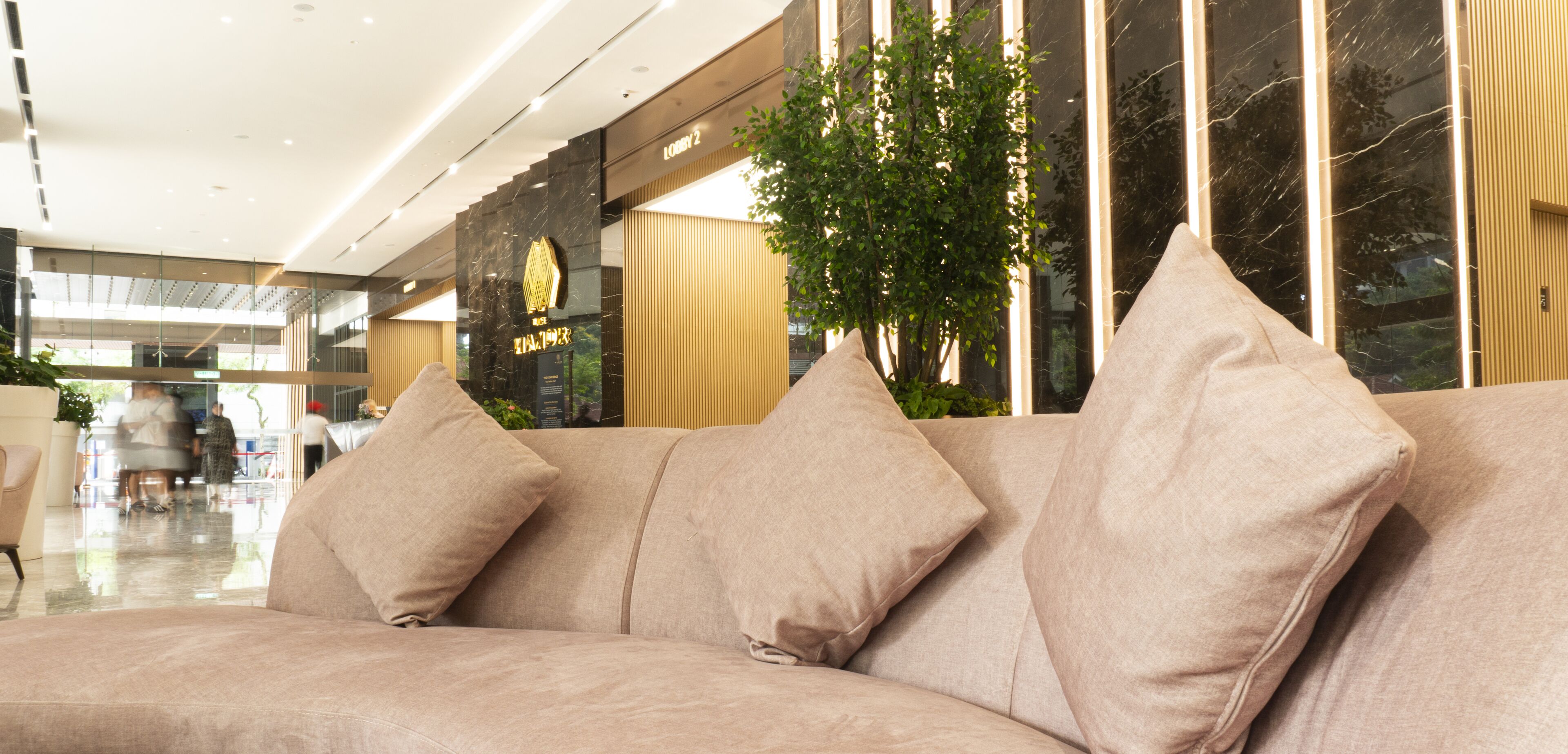 A modern hotel lobby with a beige sofa, a large mirror, and a potted plant.