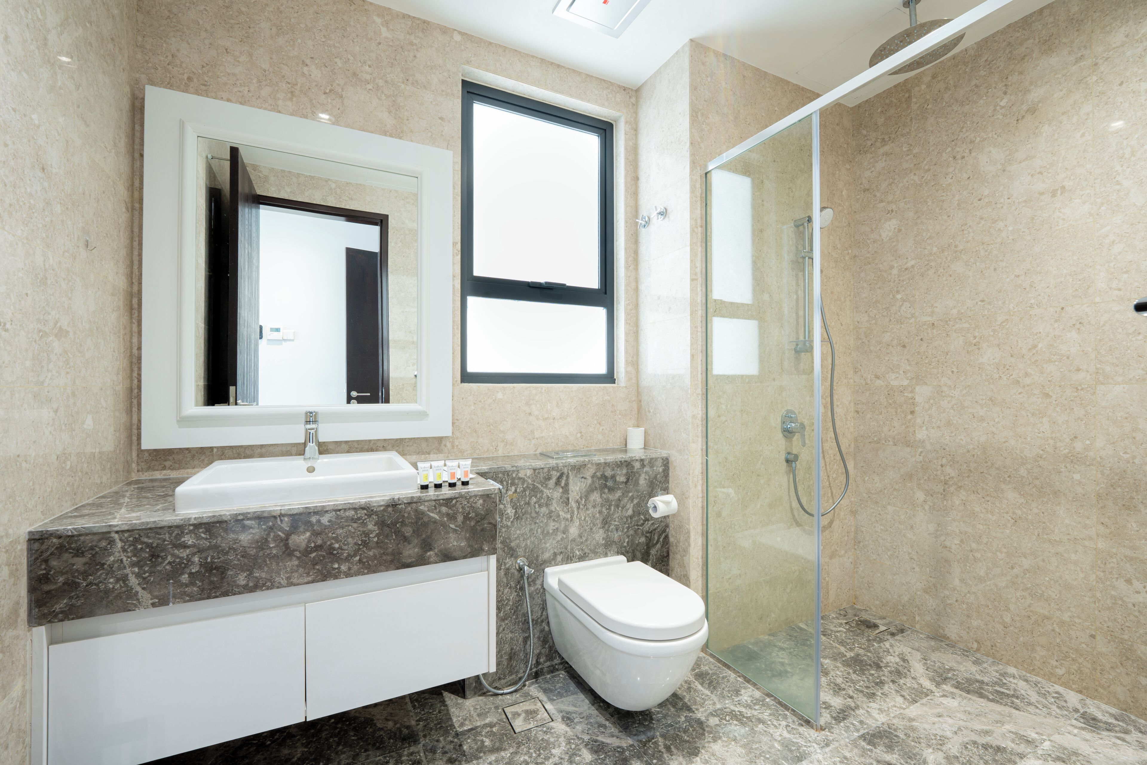 A modern bathroom with a marble countertop, a white sink, a toilet, and a glass-enclosed shower.