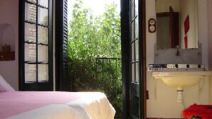 A room with a bed, a window with shutters, a sink, and a mirror.