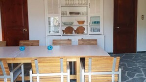 A dining area with a stone-tiled floor, a wooden table with metal chairs, and a white cabinet with glass doors displaying kitchenware.