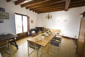 A dining area with a wooden table, chairs, and a chandelier. There is a window with blinds, a door, and a wall clock. - 'Villa Rubia' luxurious beachfront  house-chic Mediterranean Cadaques  (Cadaqués)