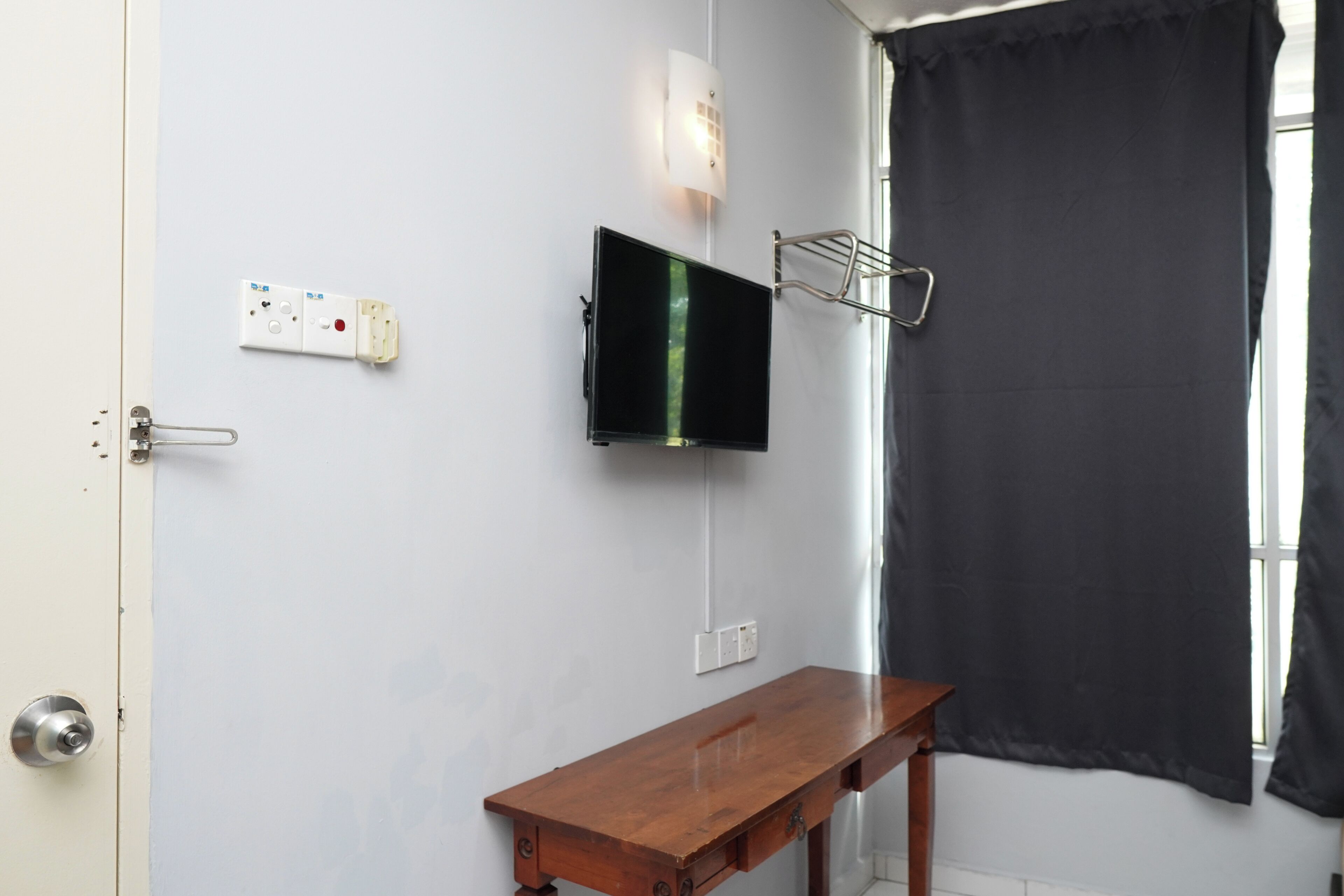 Een badkamer met een houten bankje, een wandtelevisie en een zwart gordijn.