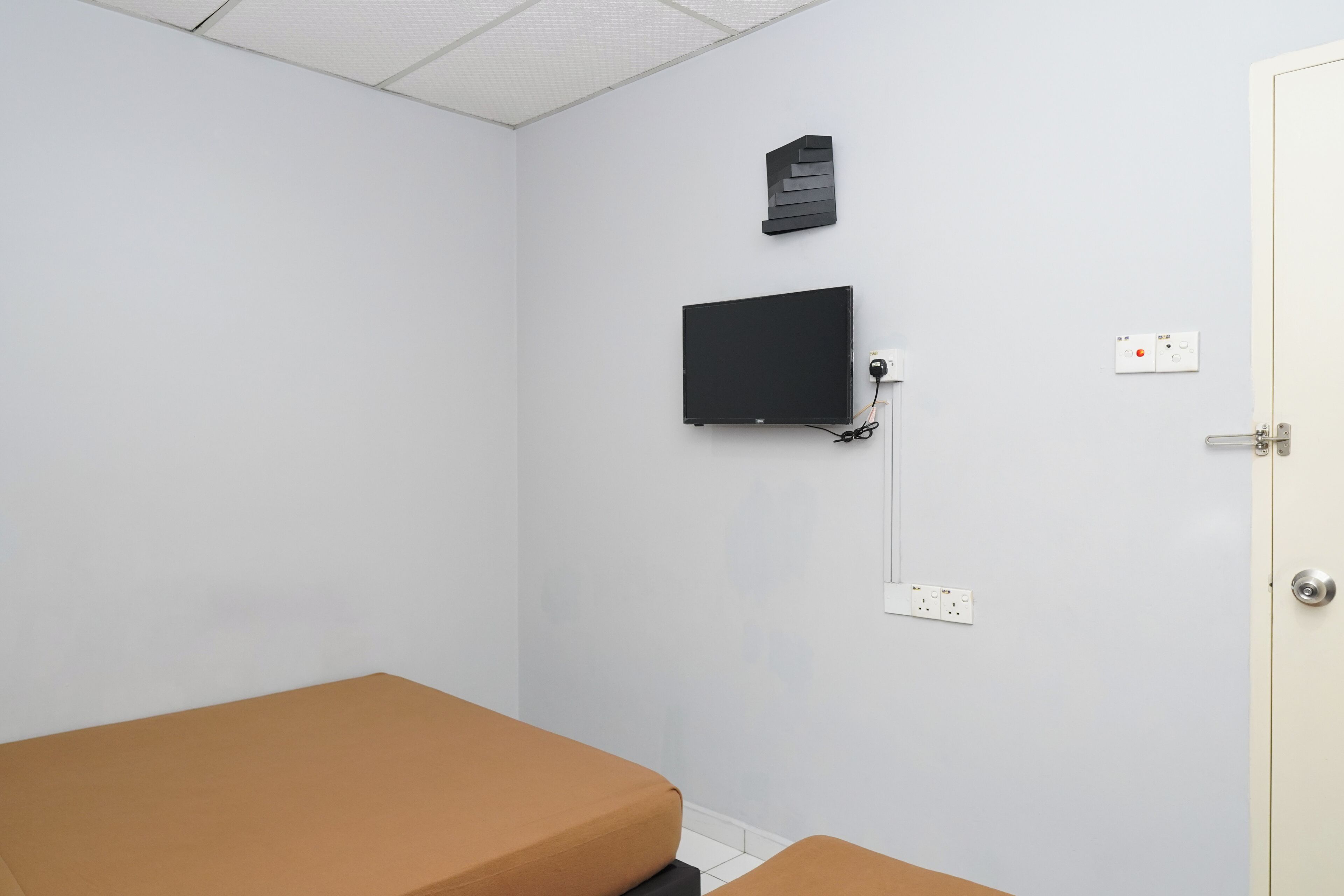 Une chambre avec un lit, un téléviseur à écran plat fixé au mur et une porte dotée d’une poignée.