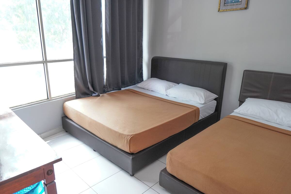 A hotel room with two beds, a window with curtains, and a desk.