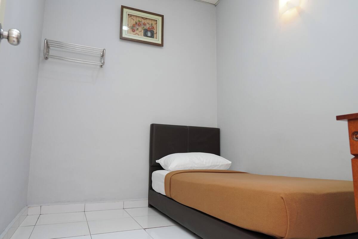 A single bed with a dark headboard, white pillows, and a brown bedspread in a room with white walls and a tiled floor.
