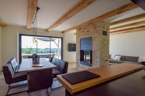 Cozy seating area surrounds a stone fireplace, with a sofa and dining table for two, and a large window offering a view of the surrounding landscape.