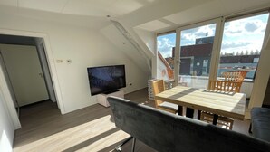Un salon moderne doté d’un téléviseur à écran plat, d’un plancher en bois, d’un canapé gris et d’un coin repas avec une table et des chaises en bois.
