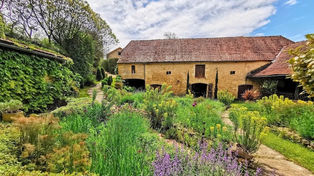 A traditional stone building with a tiled roof, surrounded by a well-maintained garden with various plants and flowers. - La Fermette au Banquet, Les Eyzies (Les Eyzies)