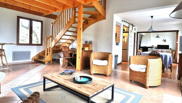 A spacious living area with a wooden staircase, wicker furniture, and a dining area with a table and chairs. - Seafront house with garden in Groix (Groix)