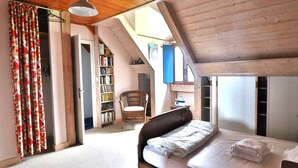 A bedroom with a sloped ceiling, a bed, a chair, a bookshelf, and a wardrobe. - Seafront house with garden in Groix (Groix)