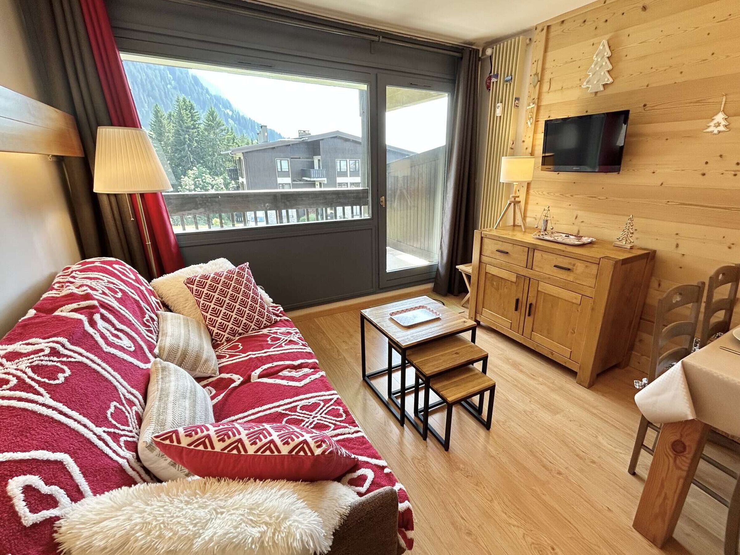 Une pièce confortable avec un canapé, une petite table, un meuble en bois et un téléviseur fixé au mur.