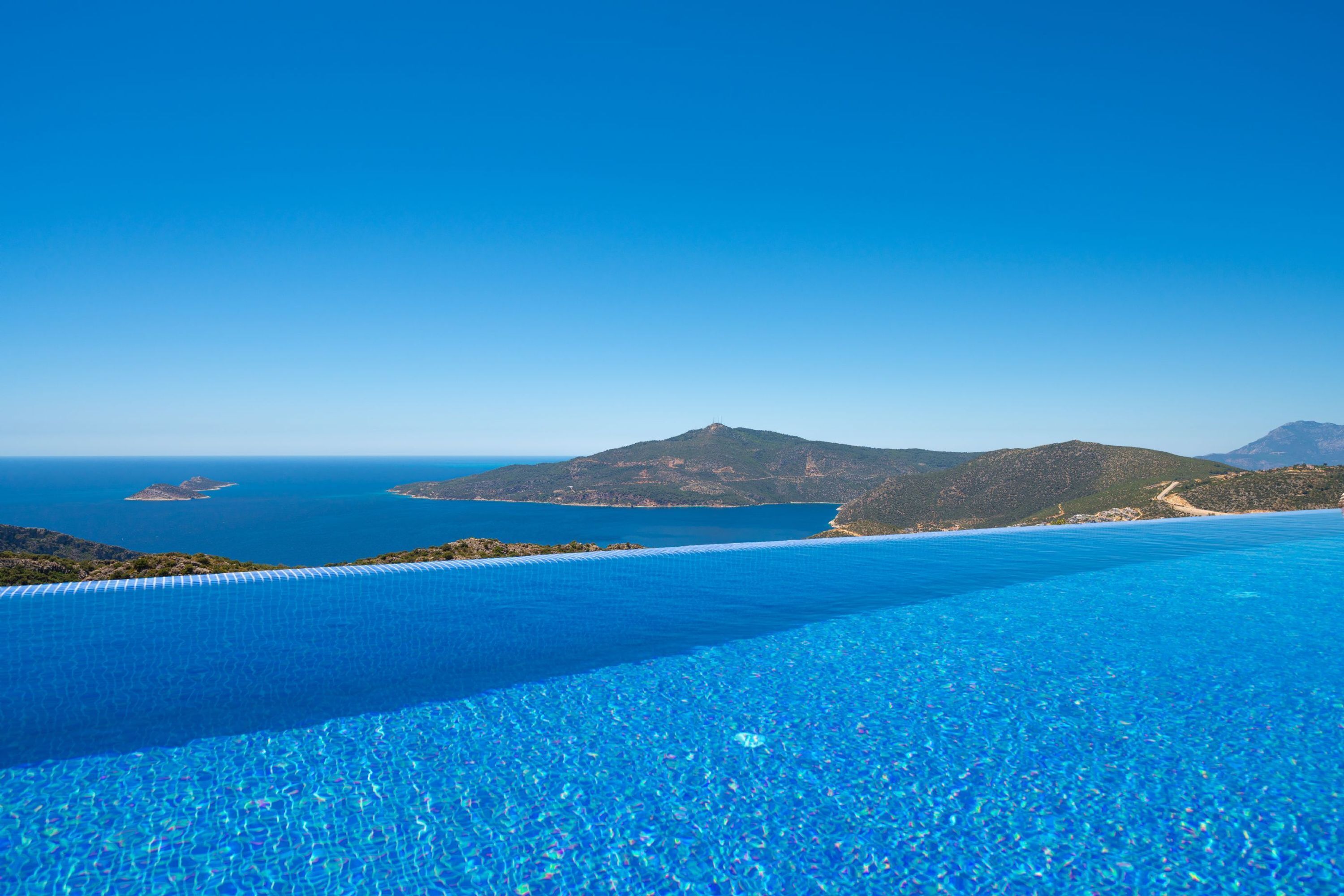 A clear blue pool with a view of the sea and distant mountains.