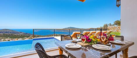 A dining table set for two with a view of the sea and mountains.