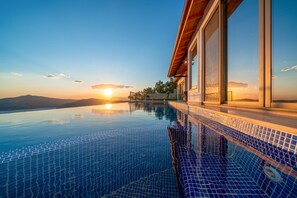 Ein moderner Infinity-Pool mit freiem Blick auf den Sonnenuntergang über den Bergen, einer Steinmauer und einem Holzdeck.